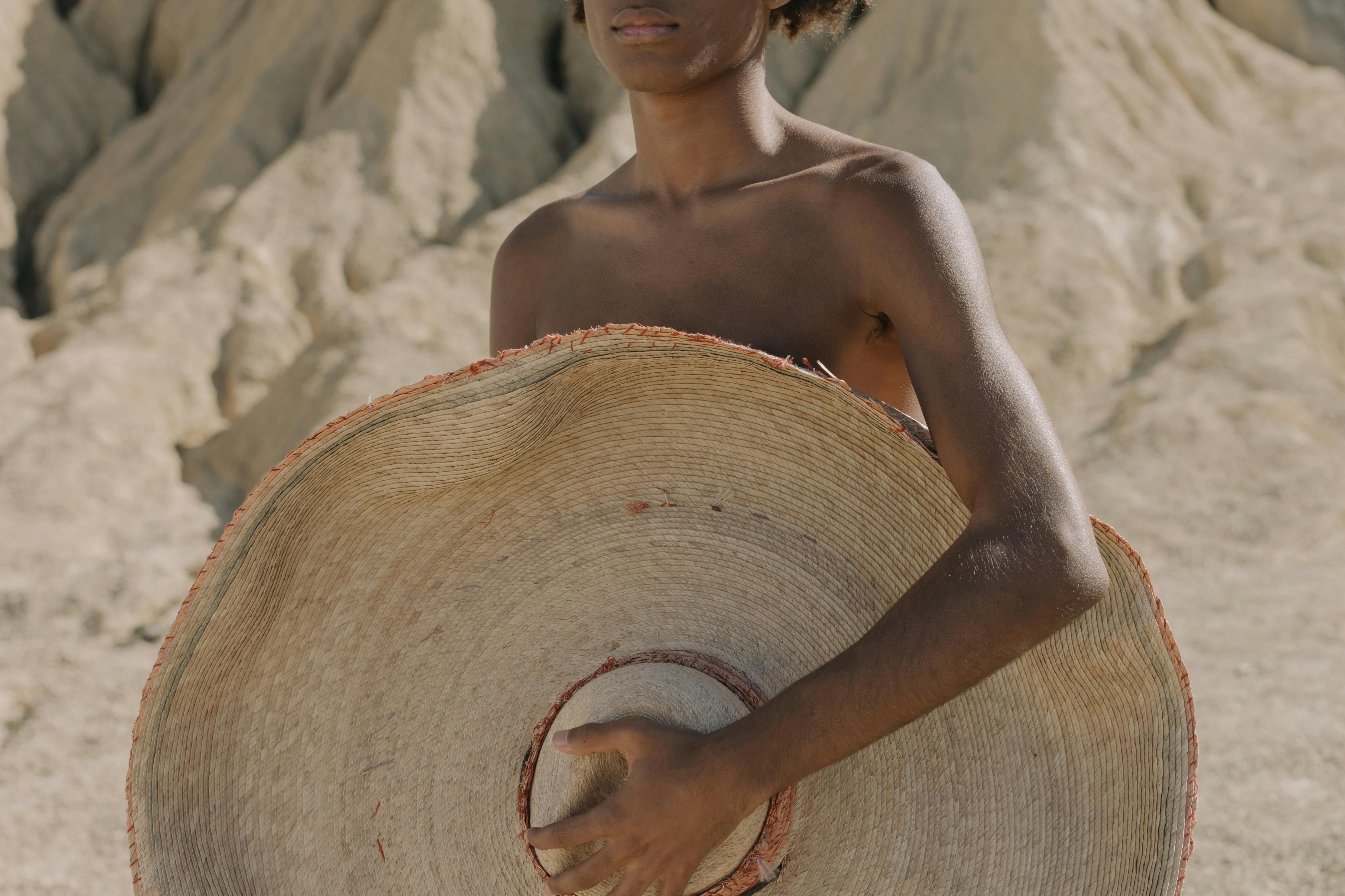 a boy shirtless boy holding a straw hat