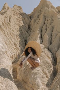 一位戴着草帽的非裔美国妇女坐在夏日阳光下的沙漠岩石上