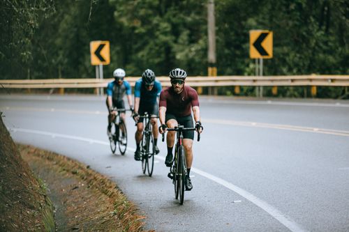Free Anonymous male cyclists in sportswear and helmets riding bicycles on fenced asphalt roadway in summer Stock Photo