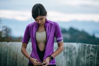 Fit female athlete zipping up sportswear near fence