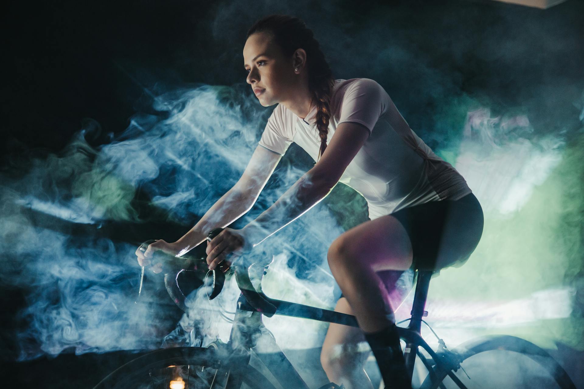 Young female athlete in active wear with concentrated gaze riding bicycle in shiny cloud while looking forward