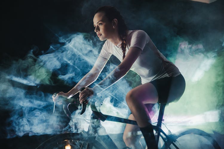 Focused Sportswoman Riding Bike In Artificial Smoke