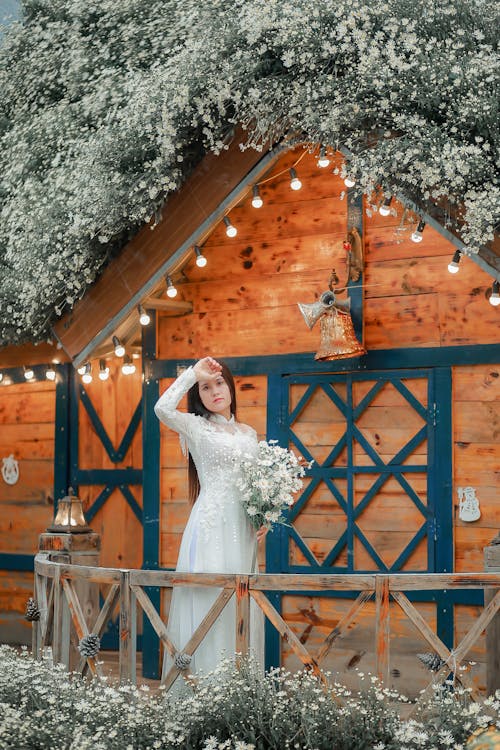 Woman in White Wedding Dress Standing Beside Brown Wooden Fence