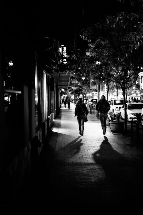 Free Black and white of anonymous people promenading on street with building and trees in evening Stock Photo