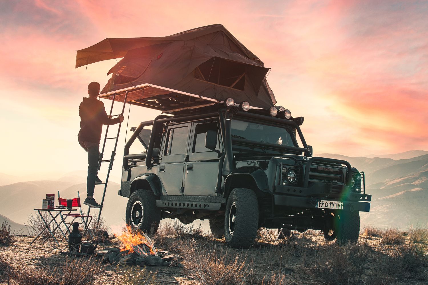 Land Rover Defender with softshell rooftop tent set up on a desert ridge at sunset for overlanding
