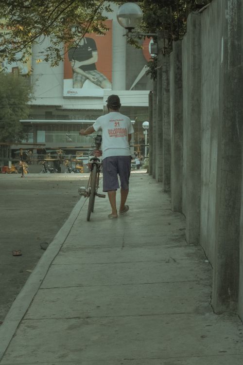 Free Back view of full body anonymous male in casual outfit walking along pavement with bike Stock Photo