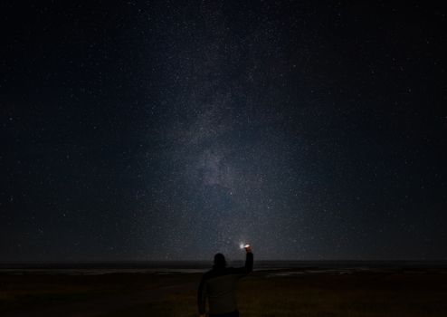 一个男人站在户外，在繁星点点的夜空下，拿着手电筒，凝视着银河