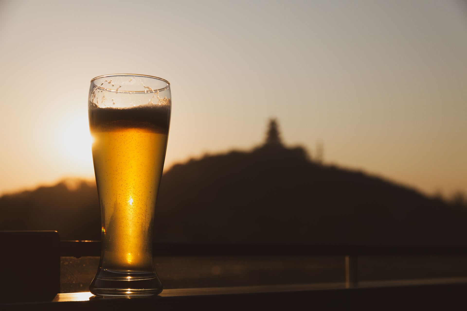A refreshing pint of beer in a glass with a sunset view in the background.