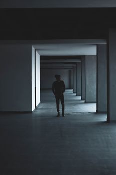 在一条极简主义风格的黑暗建筑走廊里，一个人站在重复的柱子间