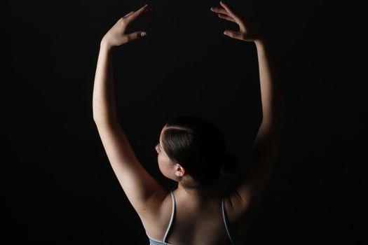 A female ballerina poses gracefully against a dark background in a dance studio, capturing movement and form.