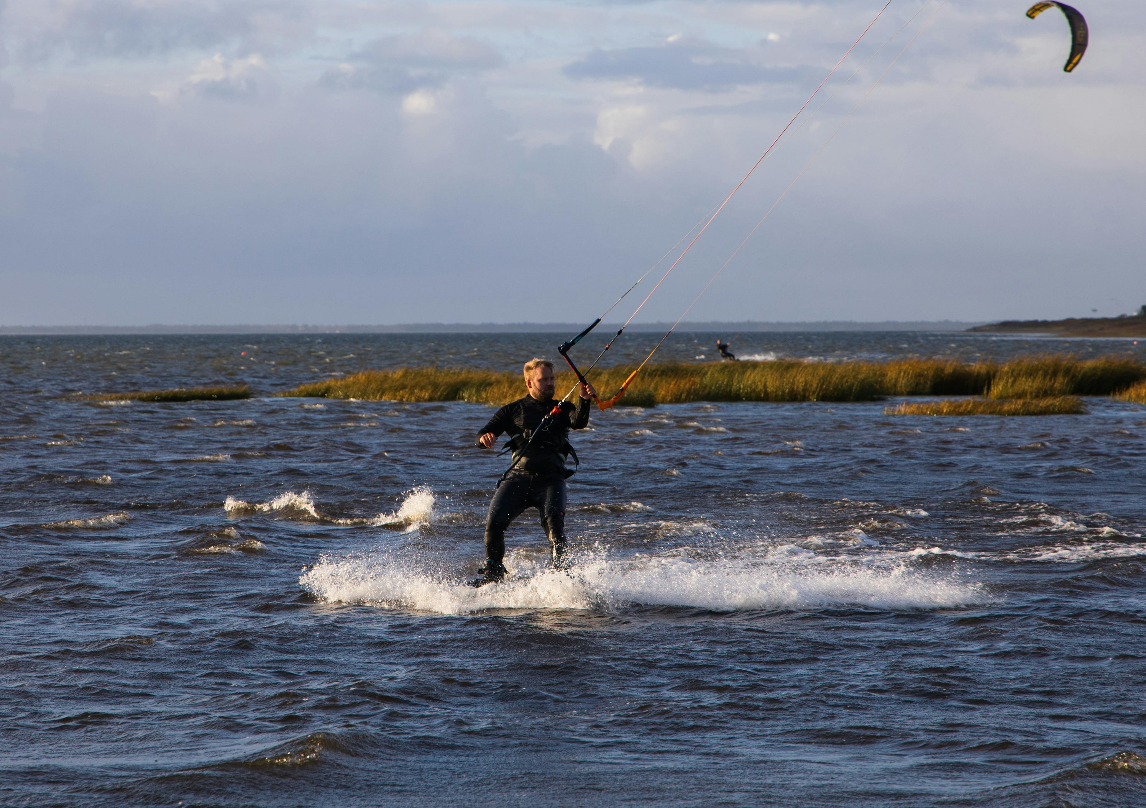 Man enjoying kitesurfing on a windy day in open water, showcasing thrilling recreation.