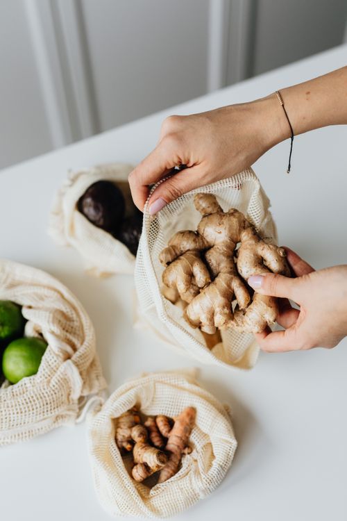 Free Hands placing ginger into an eco-friendly reusable net bag on a kitchen counter. Stock Photo
