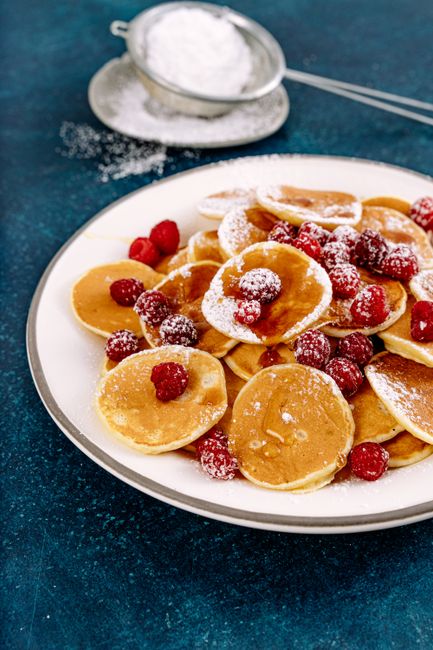 A dozen golden pancake muffins cooling on a wire rack in a muffin tin, several split open showing a tender banana-flecked crumb studded with mini chocolate chips.