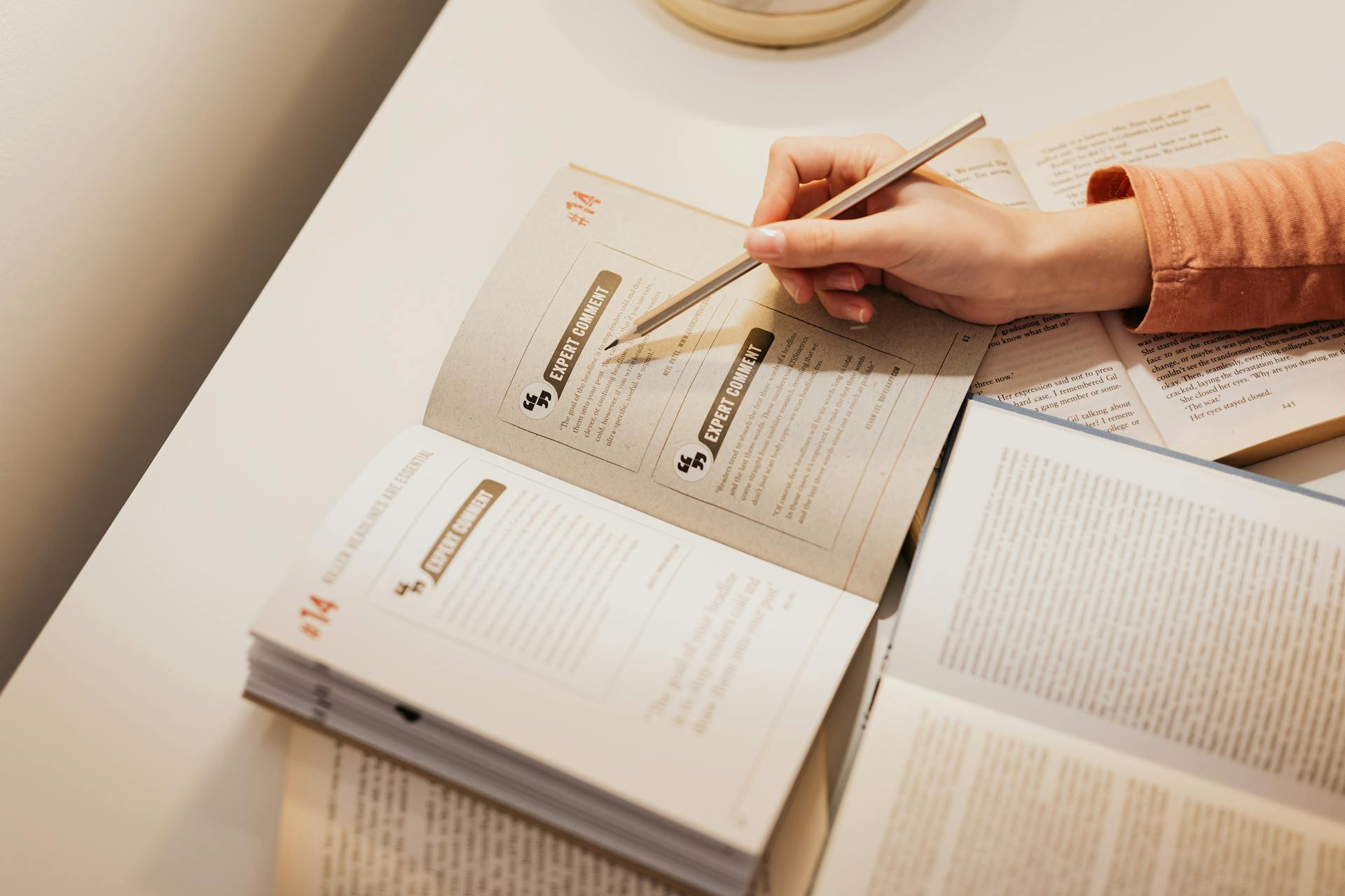 A woman using a pencil to annotate books while studying at a desk.