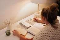 Woman Sitting at Her Desk with Open Books while Holding a Pencil