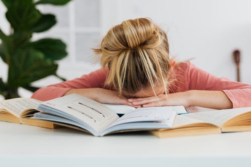 Free A young girl falls asleep on a desk surrounded by open books, illustrating study fatigue. Stock Photo