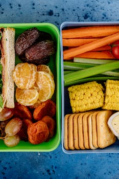 Colorful lunch boxes with assorted healthy snacks including fruits, vegetables, and sandwiches.