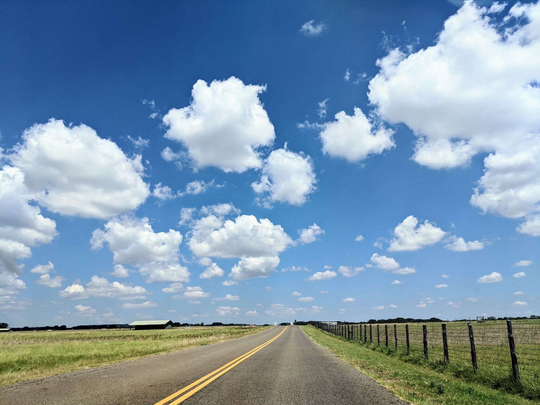 Scenic country road with white clouds in blue sky, ideal for travel and nature themes.