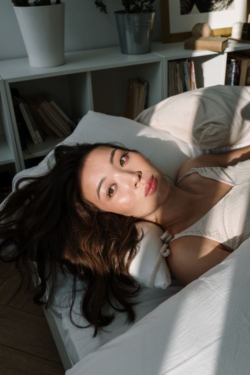 Free A serene portrait of a woman relaxing on a bed in a sunlit bedroom, capturing tranquility. Stock Photo