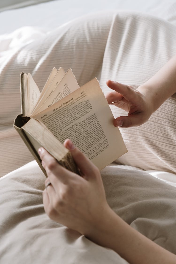 Person Holding A Book In Bed