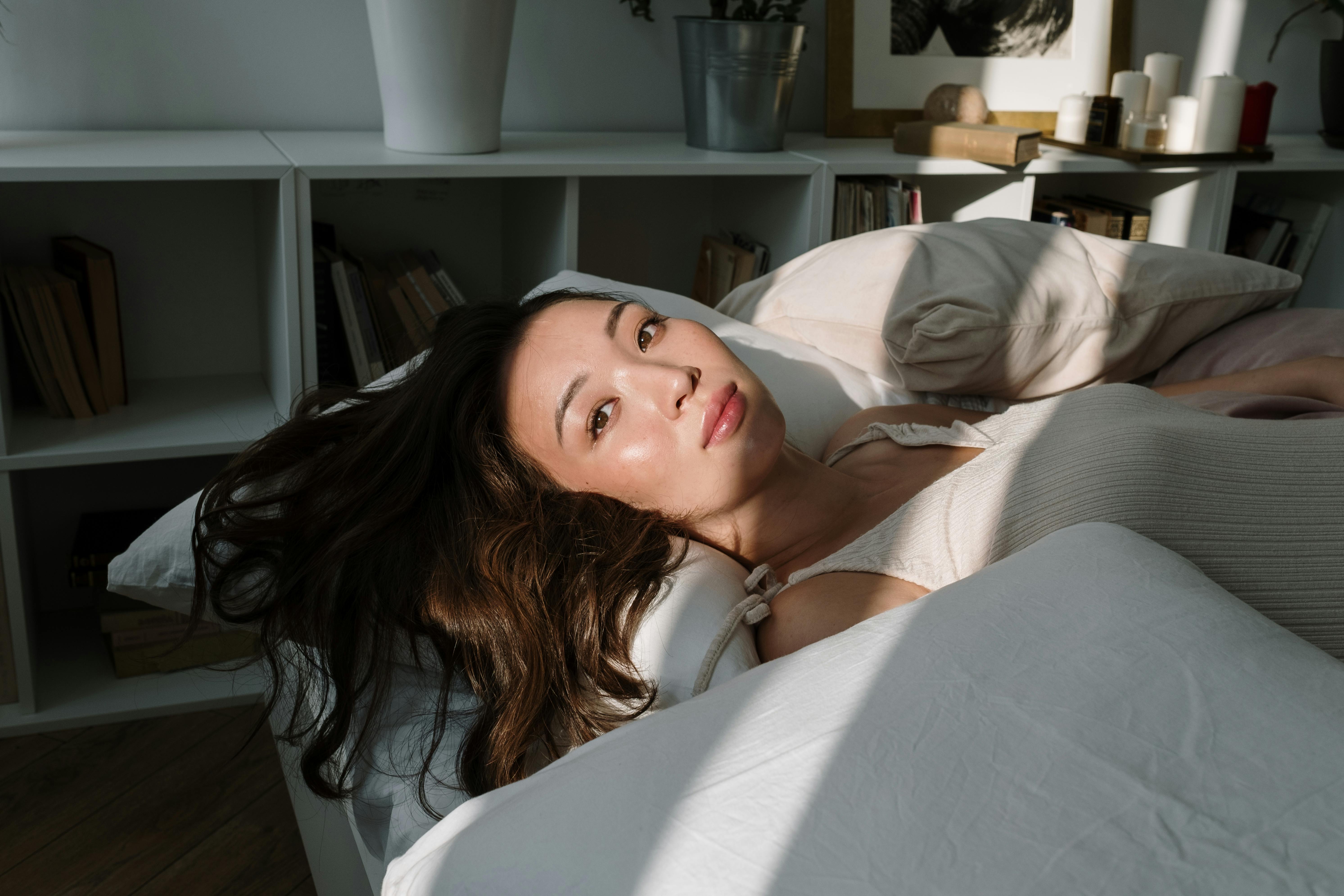 一位亚洲女性在阳光明媚的房间里，安静地躺在床上休息，显得宁静而舒适