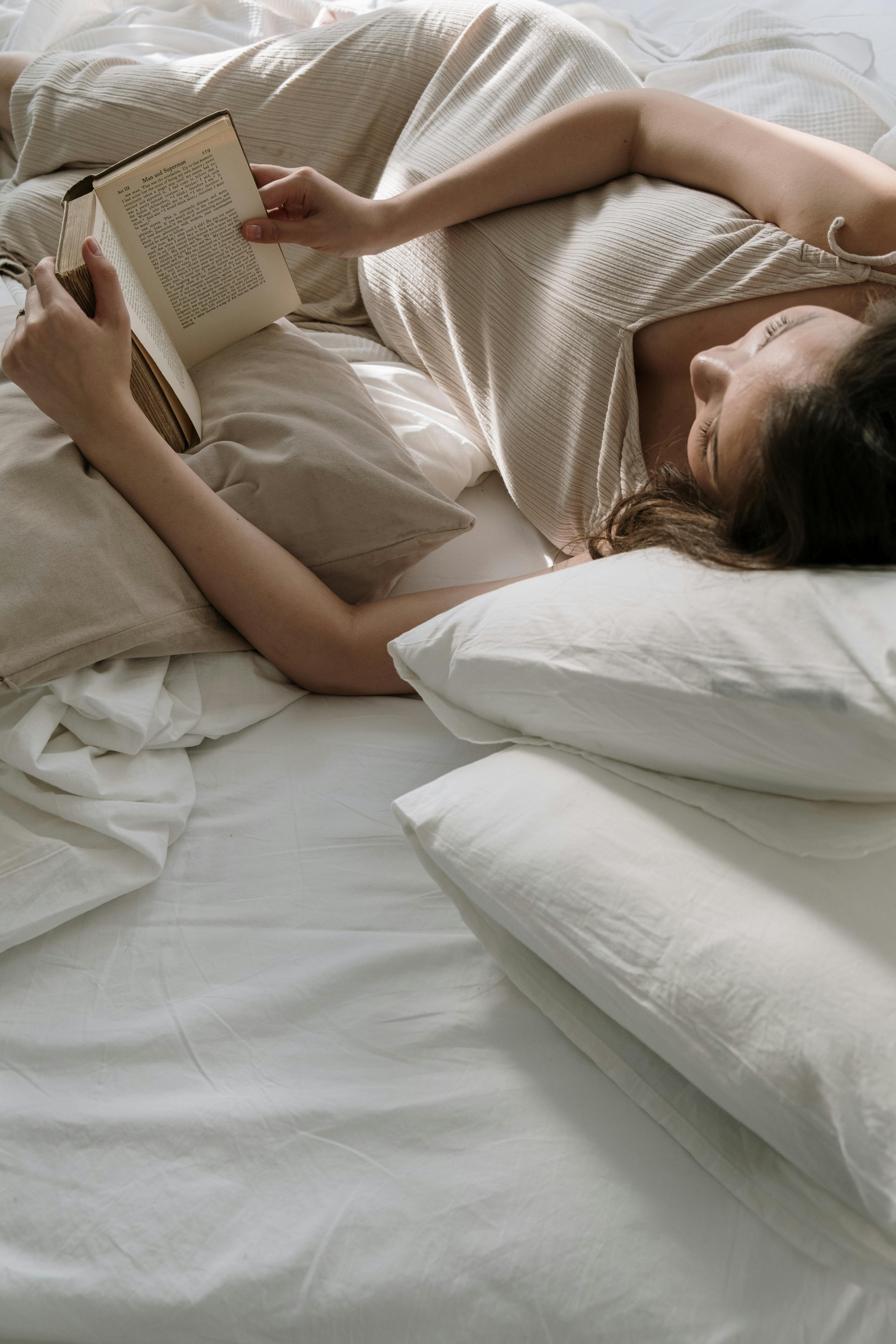 woman lying on bed with pillows reading book