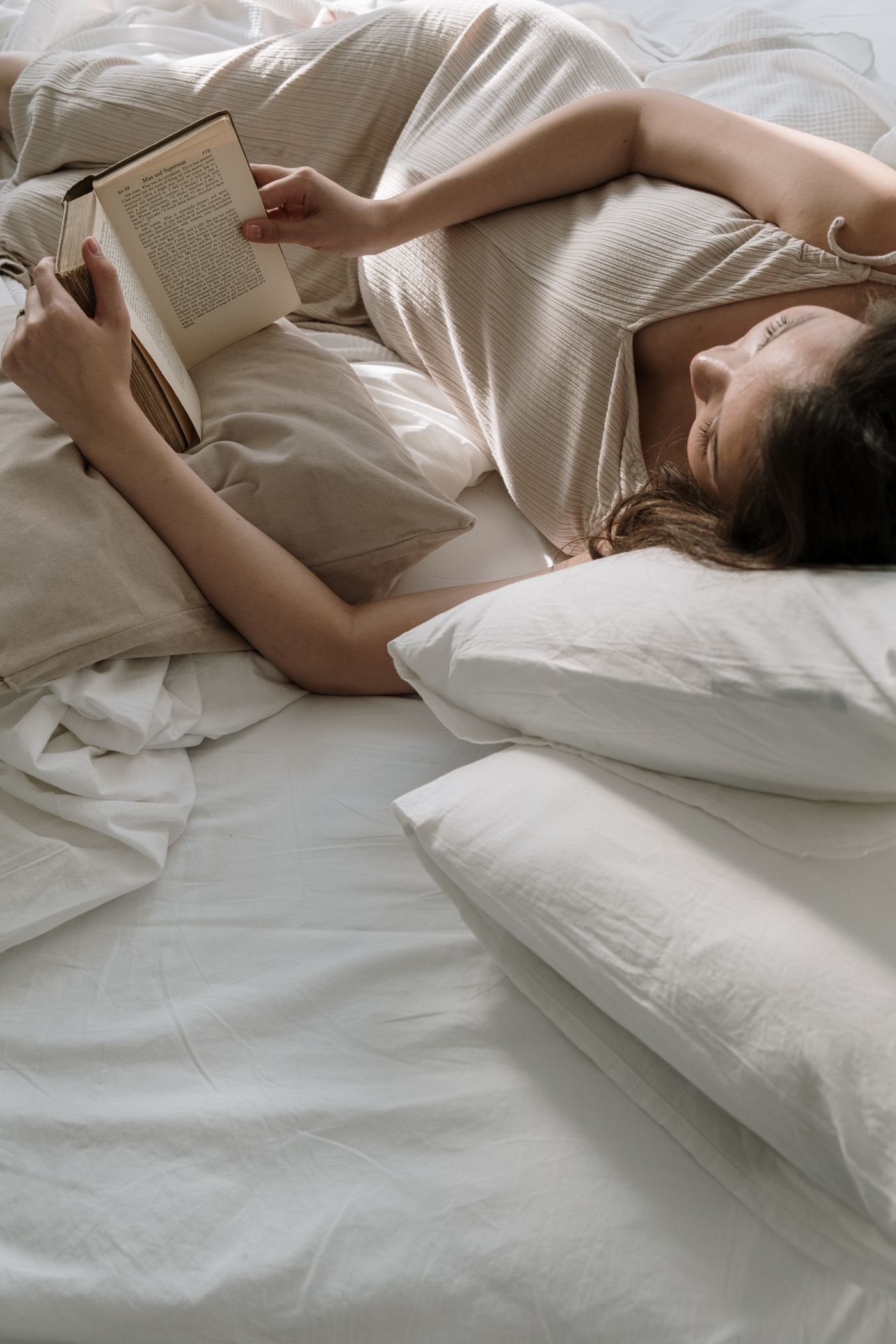 Femme enceinte lisant dans son lit avec plusieurs oreillers autour d’elle