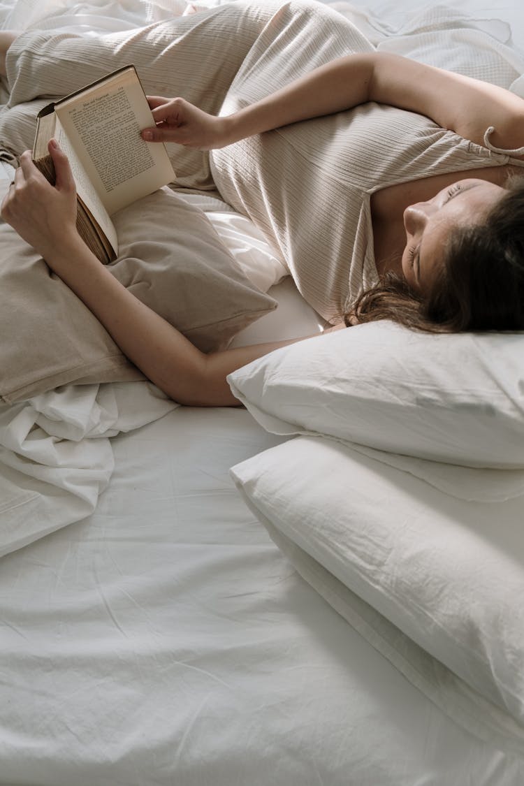 Woman Lying On Bed With Pillows Reading Book