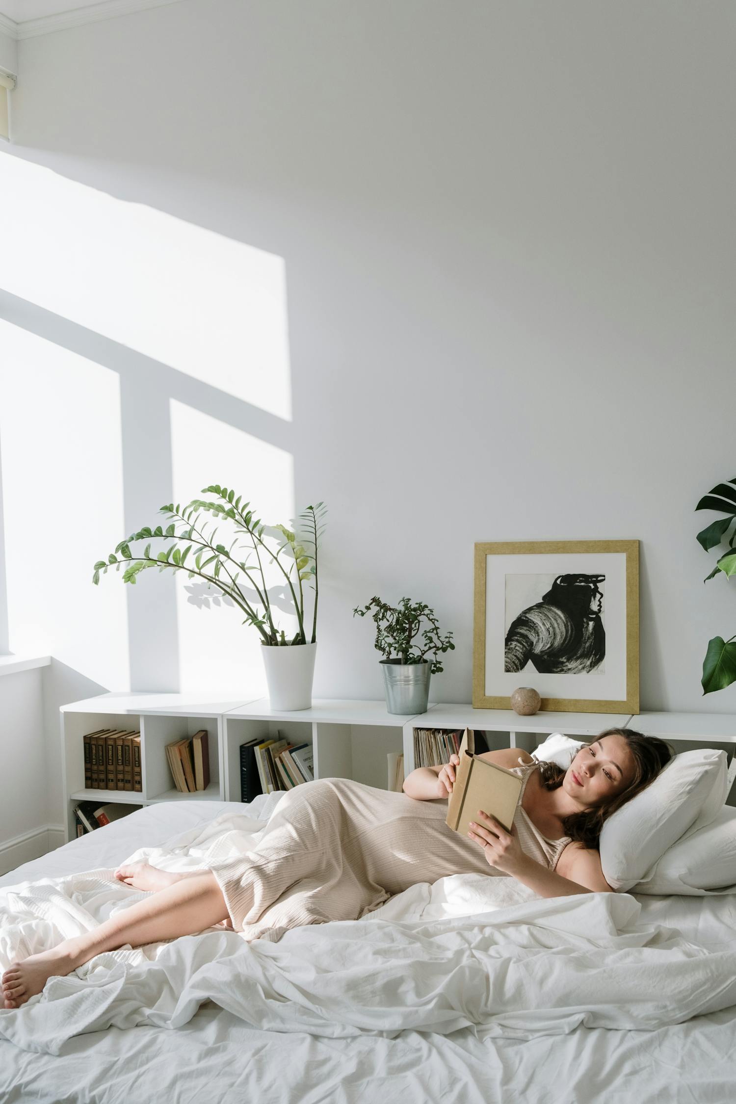 放松的女士在白色的床上做梦，戴着白色的上衣和无线耳机，在智能手机上听有声书，让她睡觉照片摄影图片_ID:356001493-Veer图库