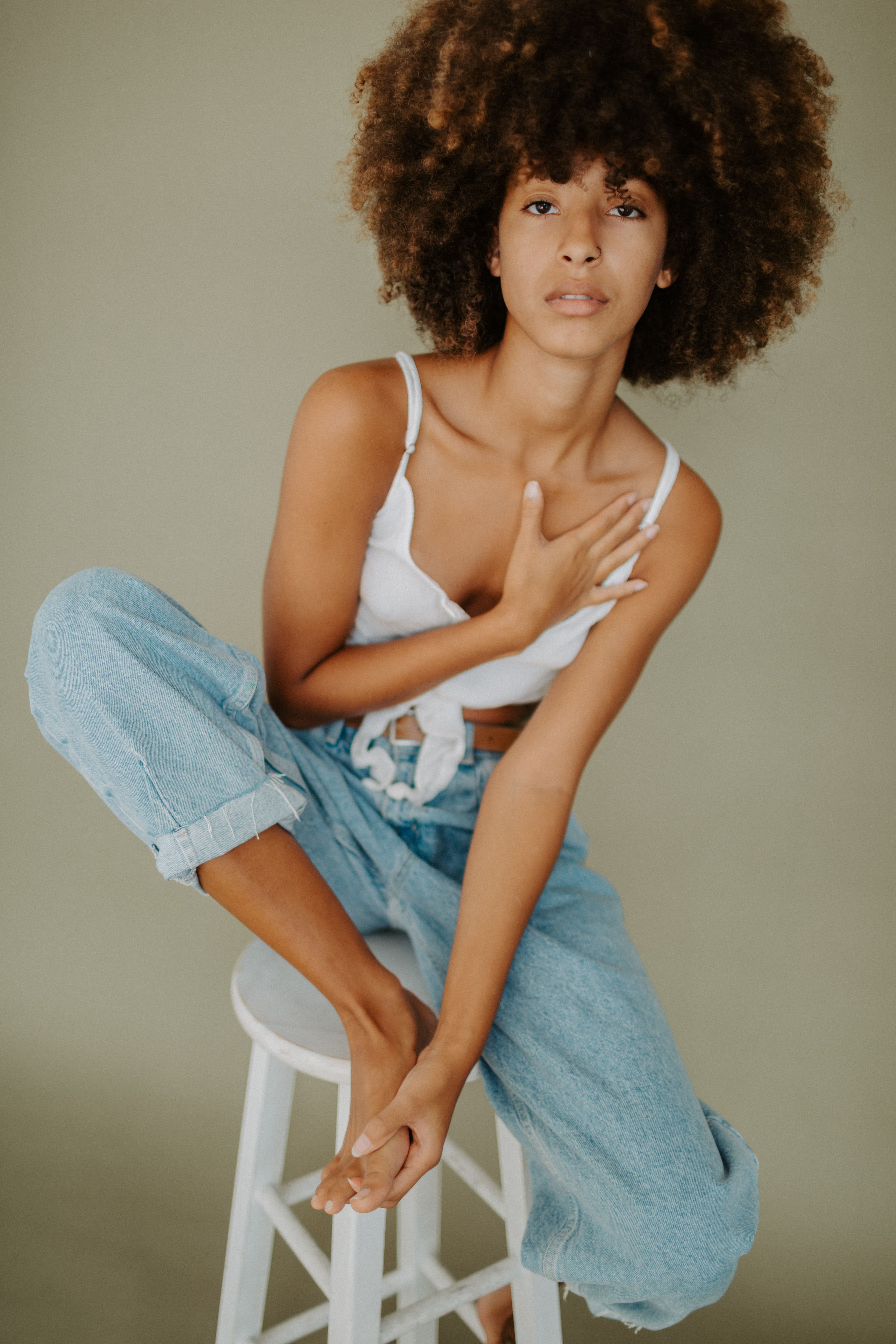 A young African American woman with afro hair posing on a chair in a studio setting.