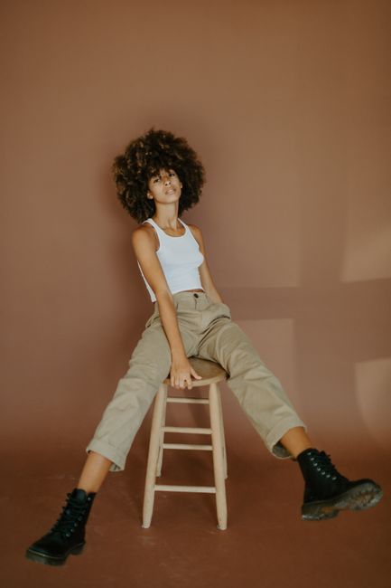 Portrait of a stylish woman with afro hair posing indoors against a brown backdrop