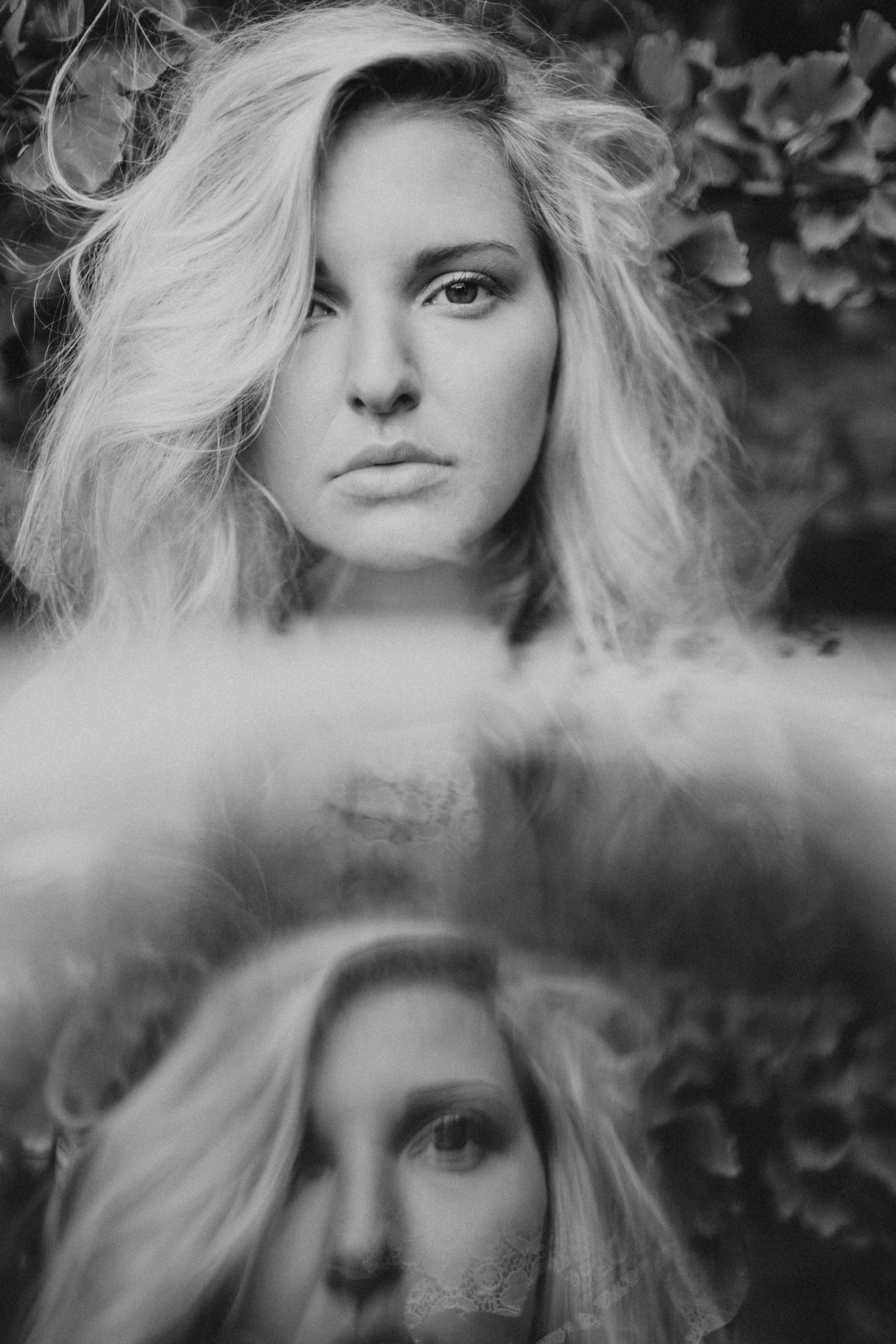 Artistic black and white portrait of a woman with mirror reflection, conveying depth and emotion.