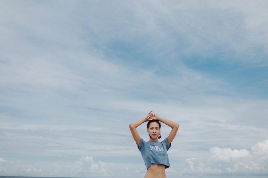 Woman in a crop top posing under a cloudy sky outdoors.