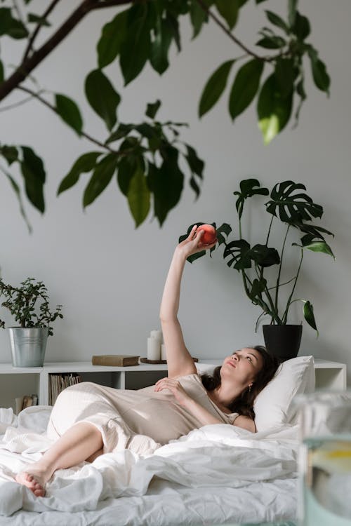 赤いリンゴの果実を保持しているベッドに横たわっている女性