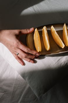 Top view of sliced oranges on a ceramic plate with hand in dappled sunlight.