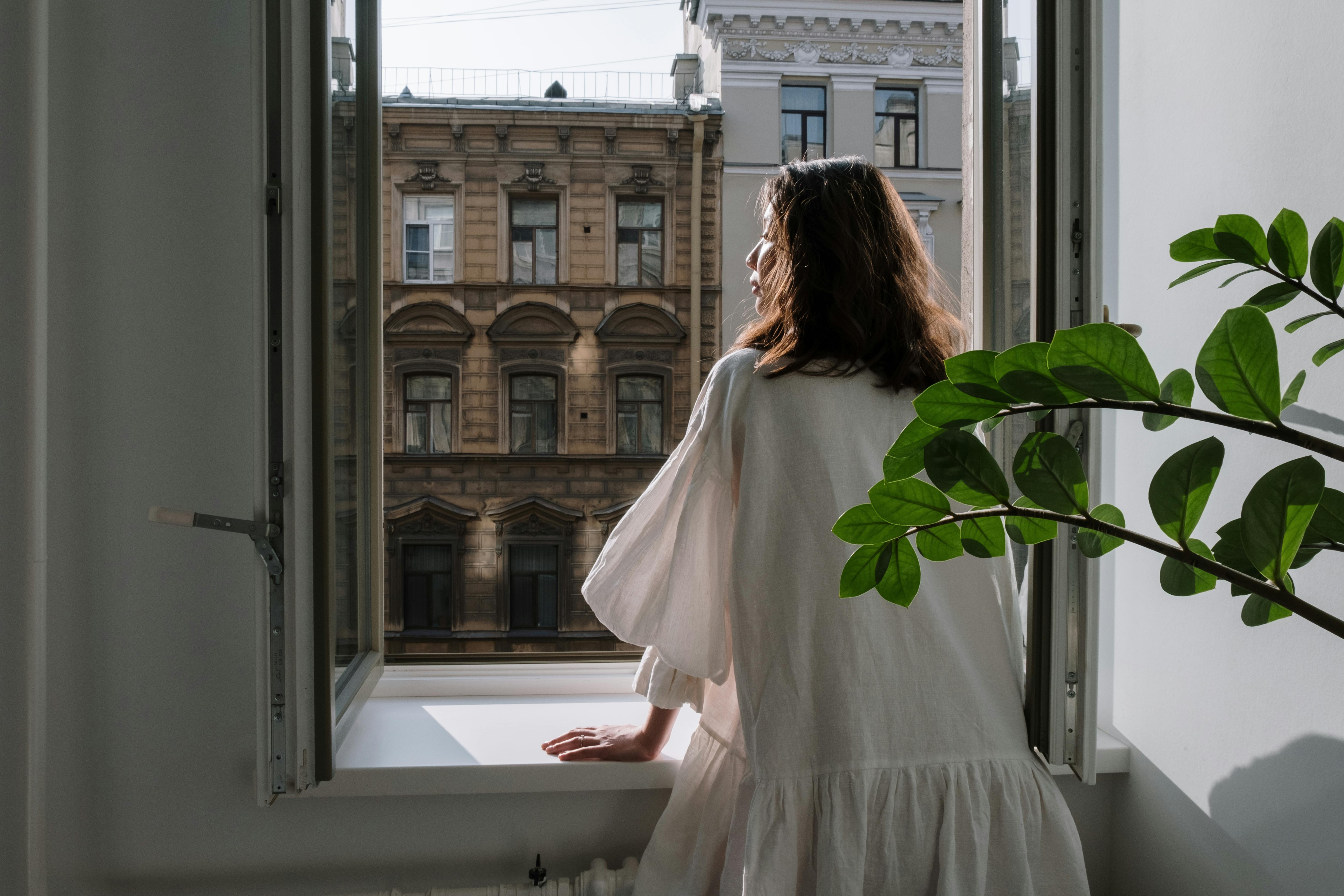 woman in white long sleeve dress standing in front of window