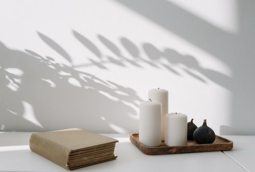 Free Elegant still life featuring candles, a book, and leaf shadows on a white tabletop. Stock Photo