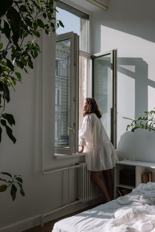 Woman in White Dress Standing by the Window