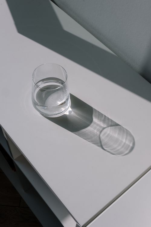 Free Minimalist photo of a glass of water casting a shadow on a white table. Stock Photo