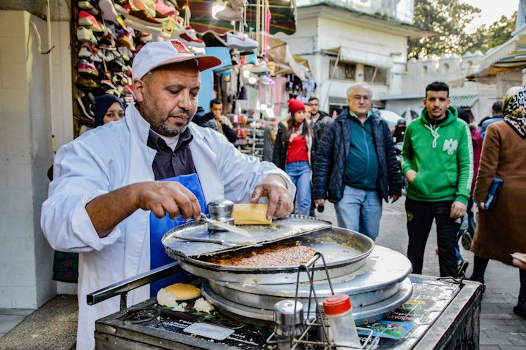 Man In White Long Sleeves Shirt And Cap Cooking On The Street