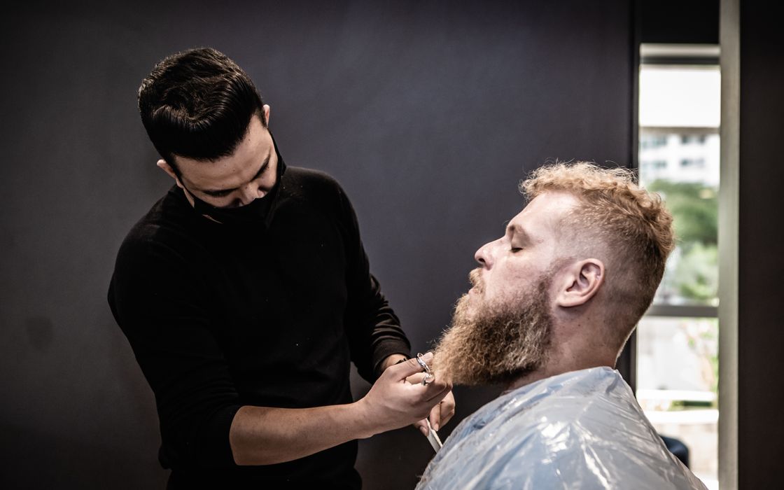 A barber professionally trims a man's beard in a modern salon.