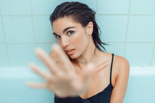 Free Young woman with freckles and wet hair in a bathtub, wearing a blue top. Intimate and serene setting. Stock Photo