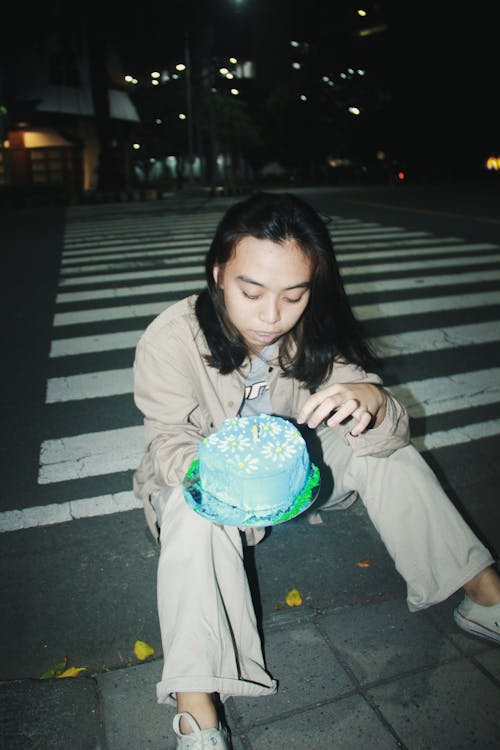 Woman Sitting on a Sidewalk at Night and Holding a Birthday Cake 