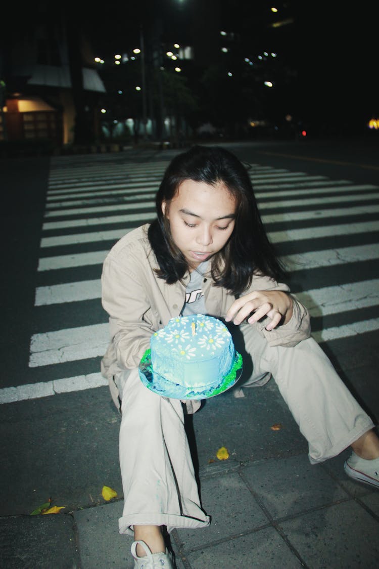 Woman Sitting On A Sidewalk At Night And Holding A Birthday Cake 