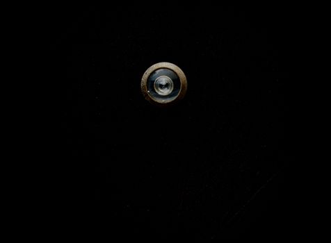 Close-up image of a metallic door peephole with a black background, offering copy space.