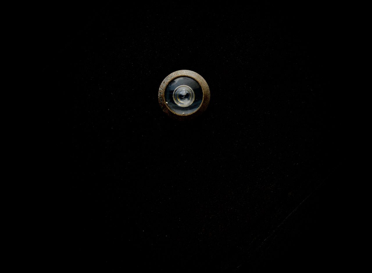 close up image of a metallic door peephole with a black background off
