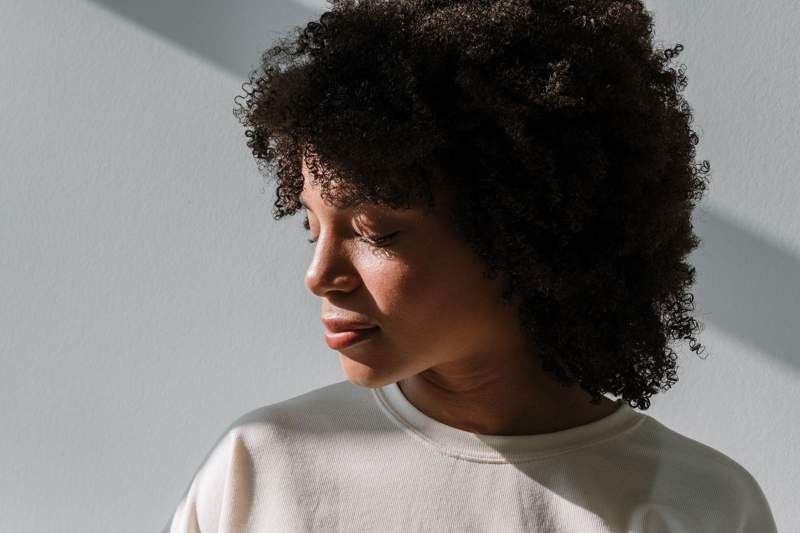 Close-up portrait of a woman with curly afro hairstyle, eyes closed in natural light.