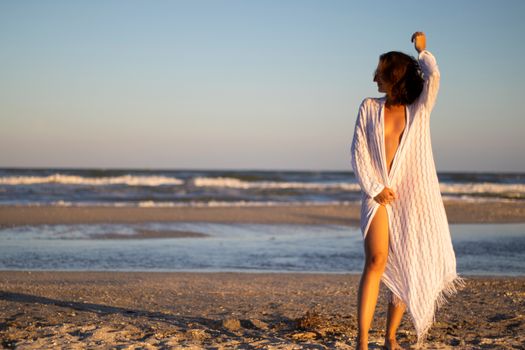 Woman in a white cover-up posing on a Romanian beach during sunset. Serene and elegant.