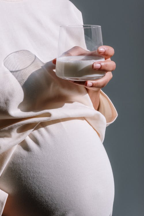Pregnant Woman in Beige Maternity Dress Holding a Glass of Milk