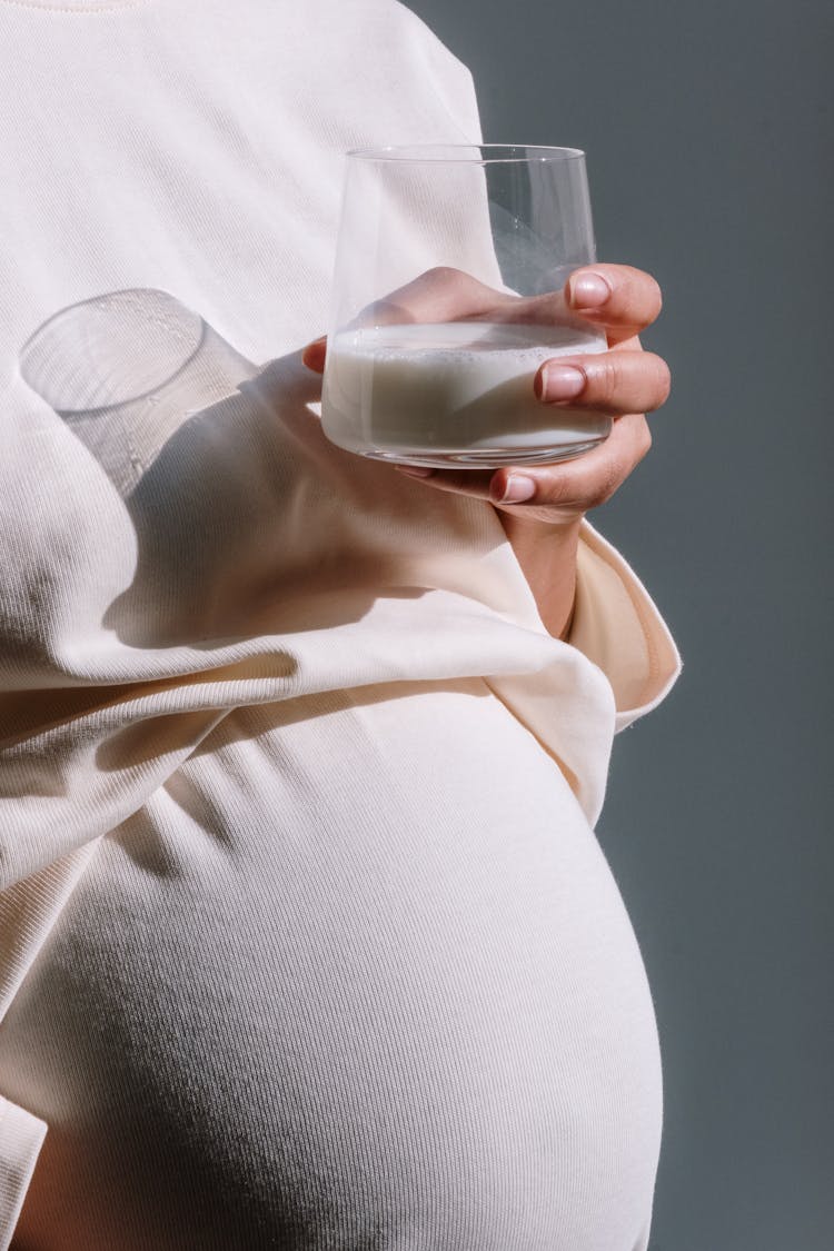 Pregnant Woman In Beige Maternity Dress Holding A Glass Of Milk